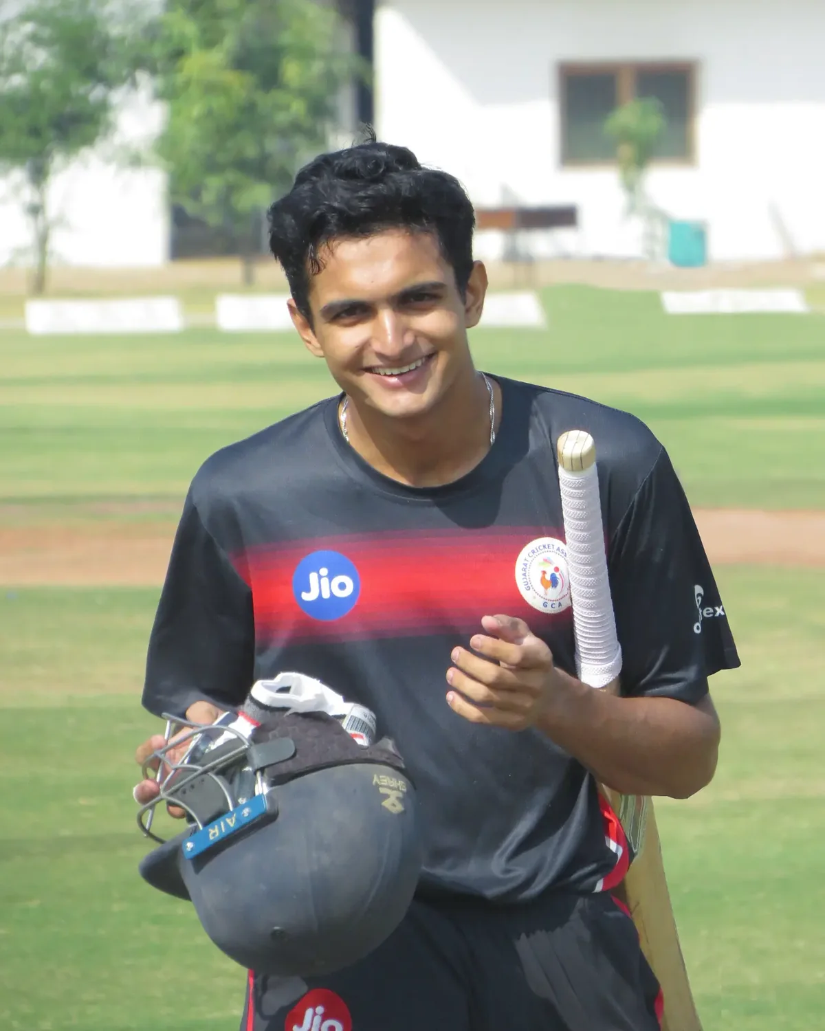 Raj Chaudhari on a cricket ground in his Gujarat kit, holding a bat and helmet